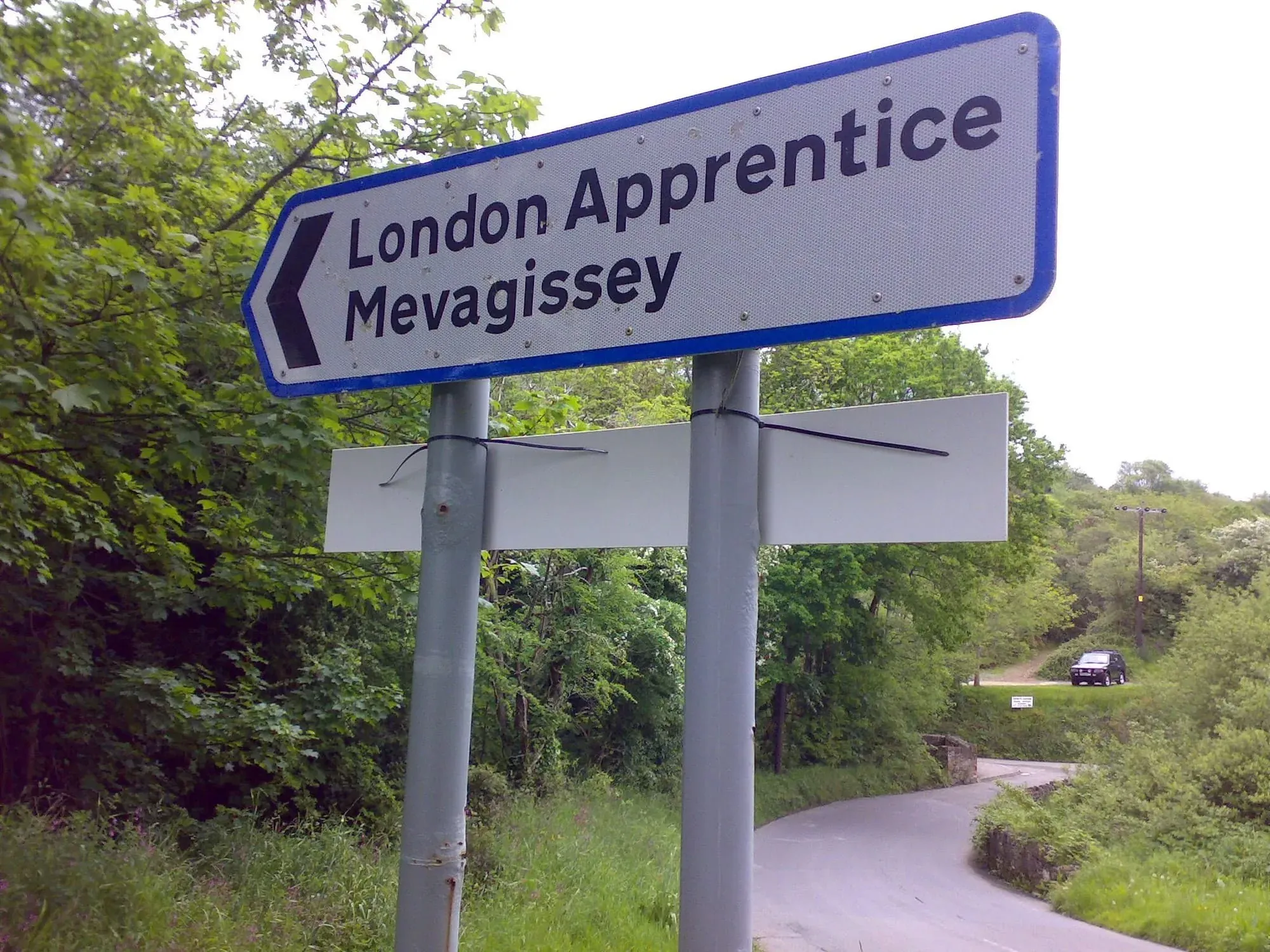 Blue directional sign pointing to London Apprentice Mevagissey along a tree-lined road