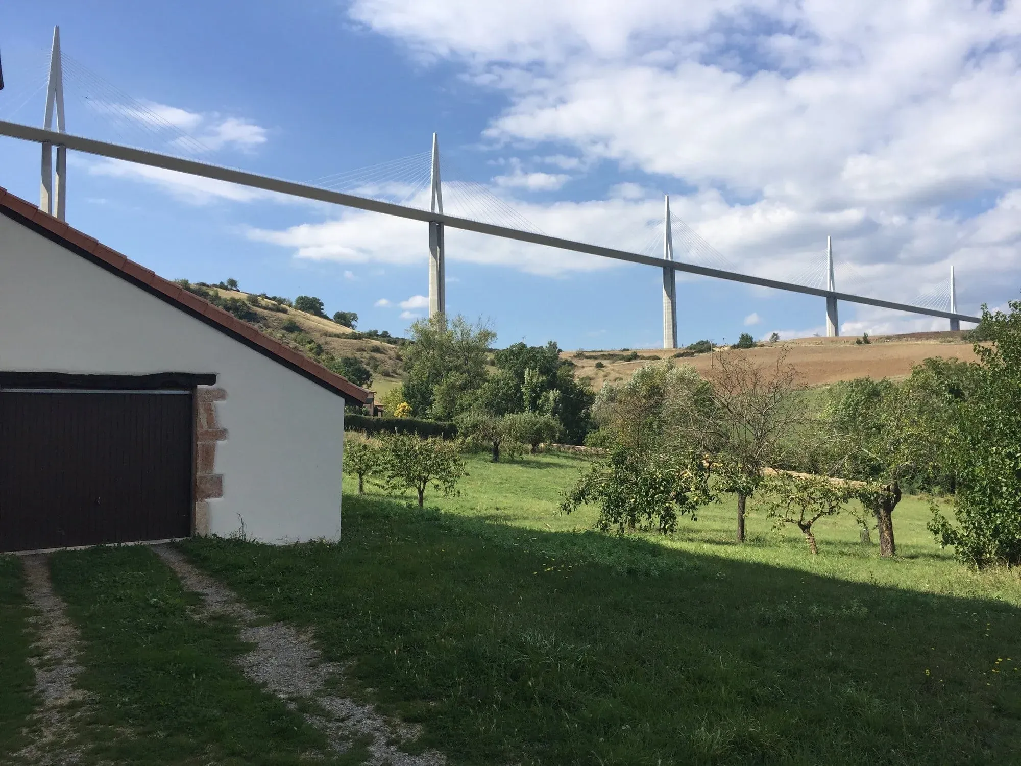 Rural cottage with Millau Viaduct bridge spanning landscape behind