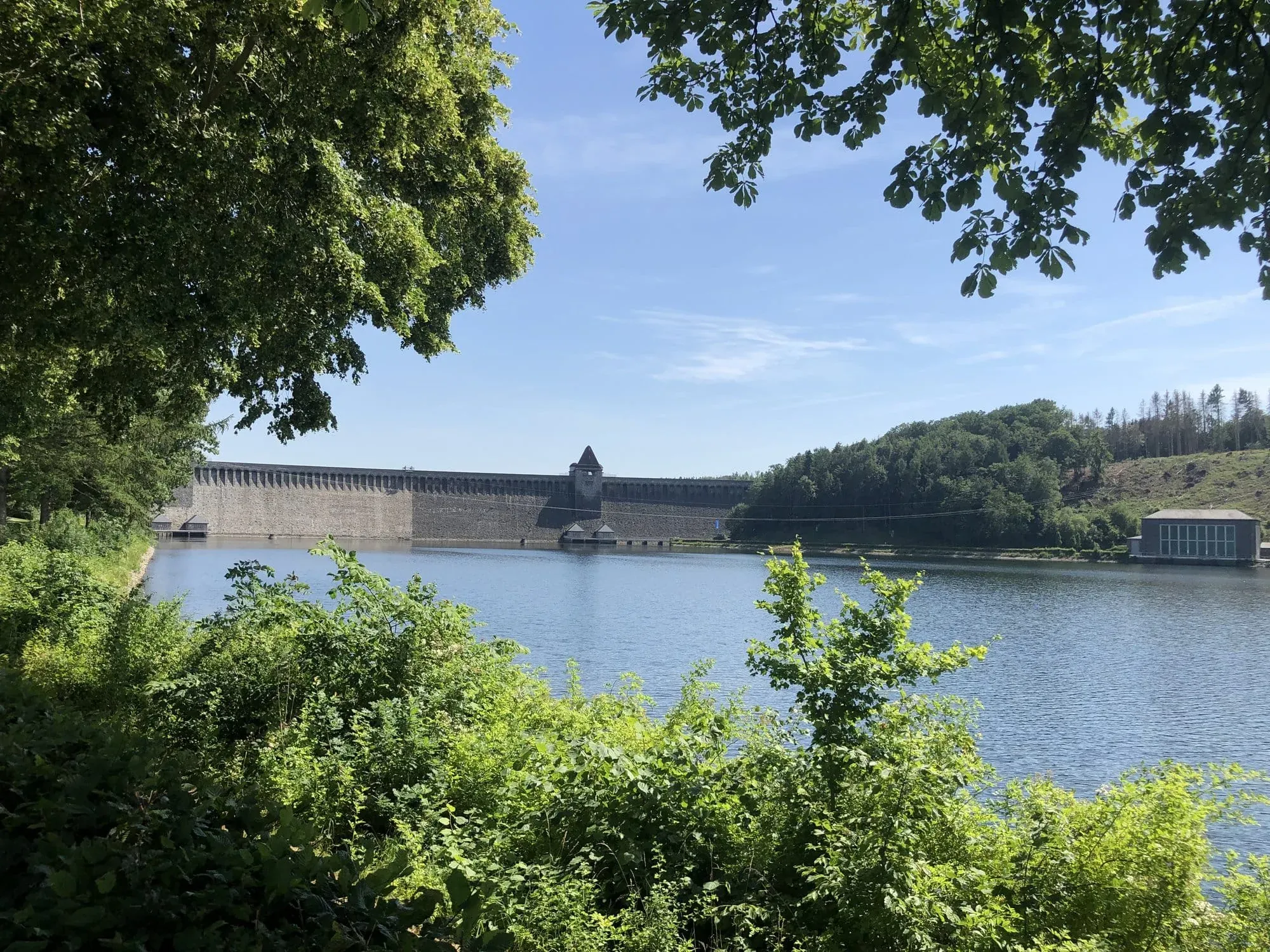 Historic stone dam across blue reservoir surrounded by green trees