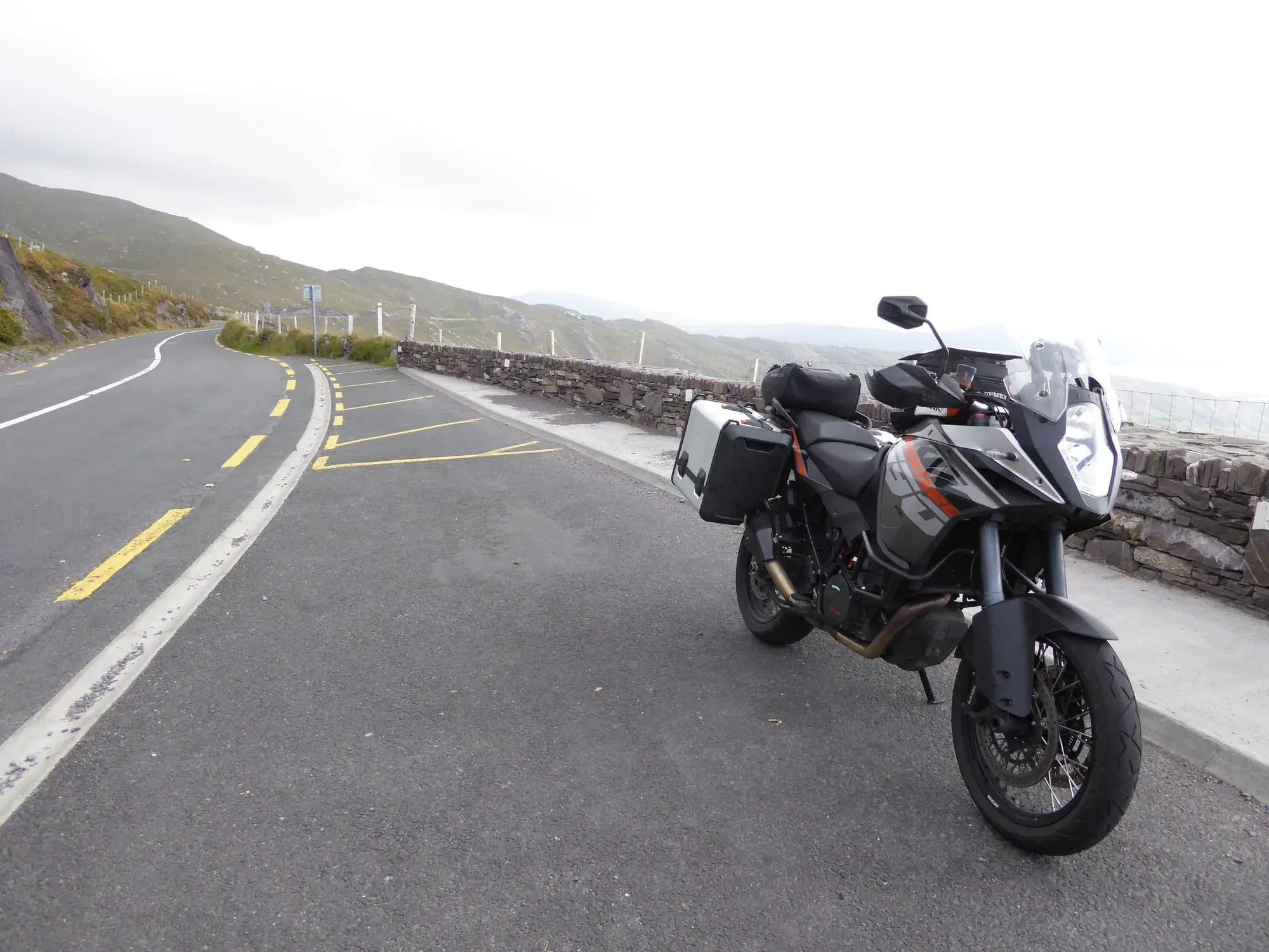 Adventure motorcycle parked on curved mountain road with valley landscape