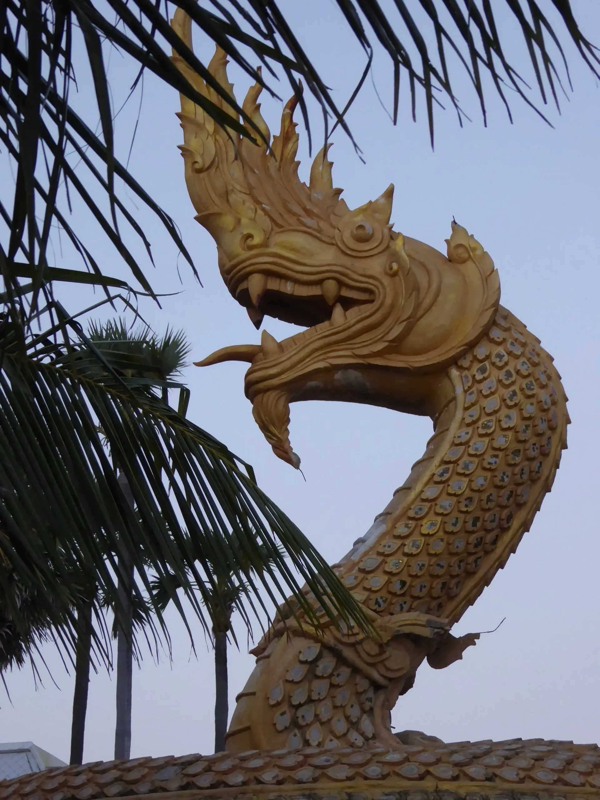 Golden carved dragon statue with intricate details against palm fronds and sky