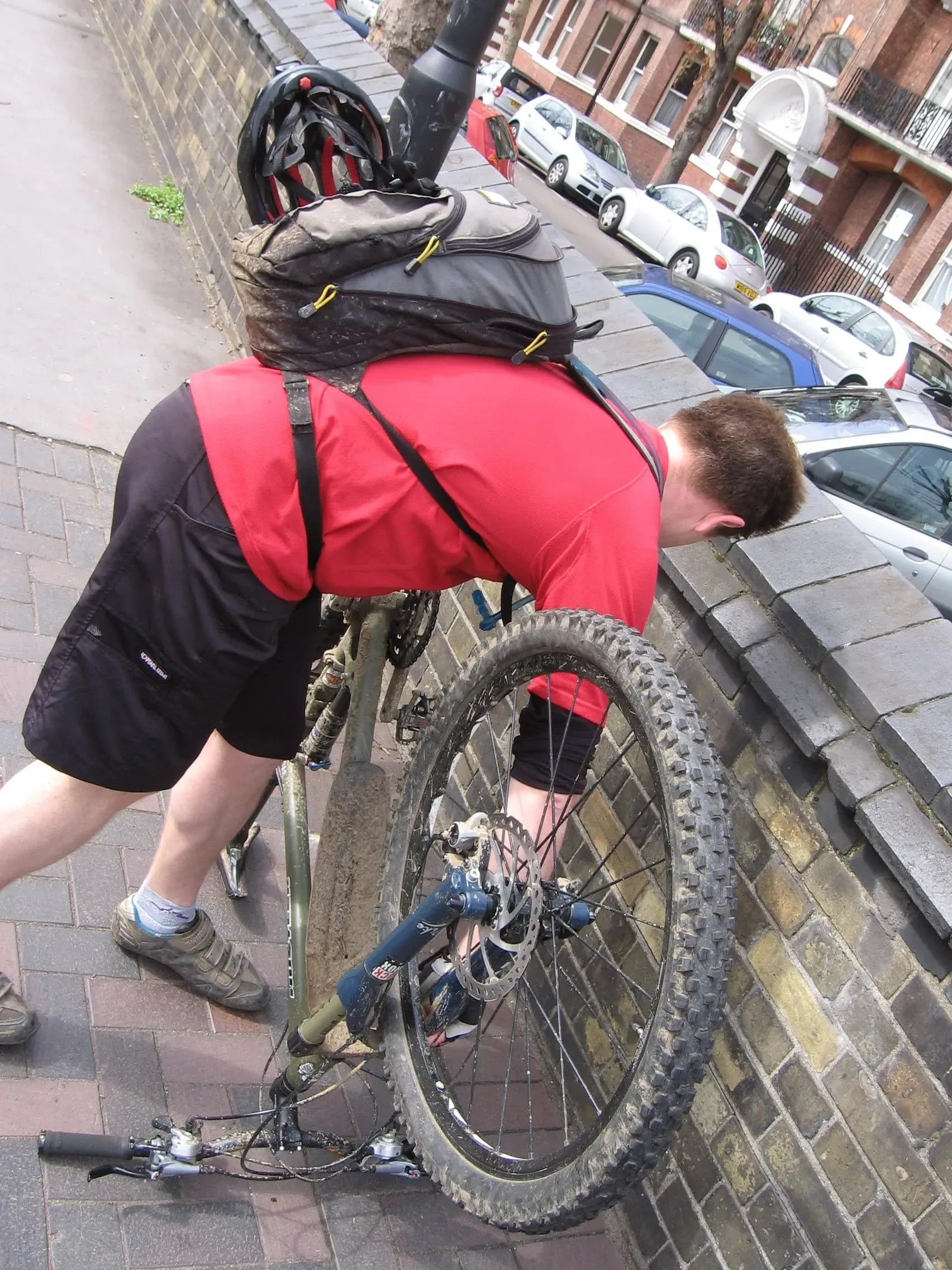 Cyclist in red vest working on mountain bike wheel on urban street