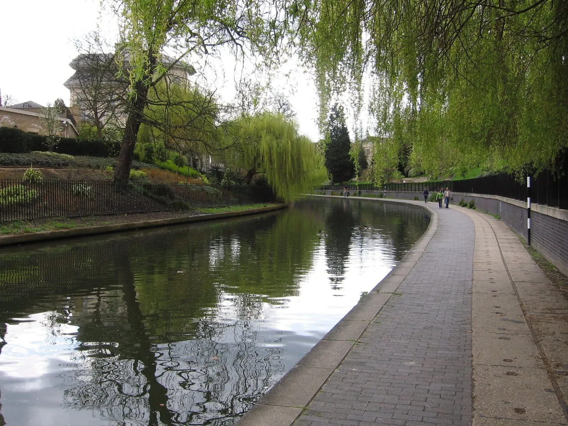 Wide tree-lined canal towpath with paved walkway and railings both sides