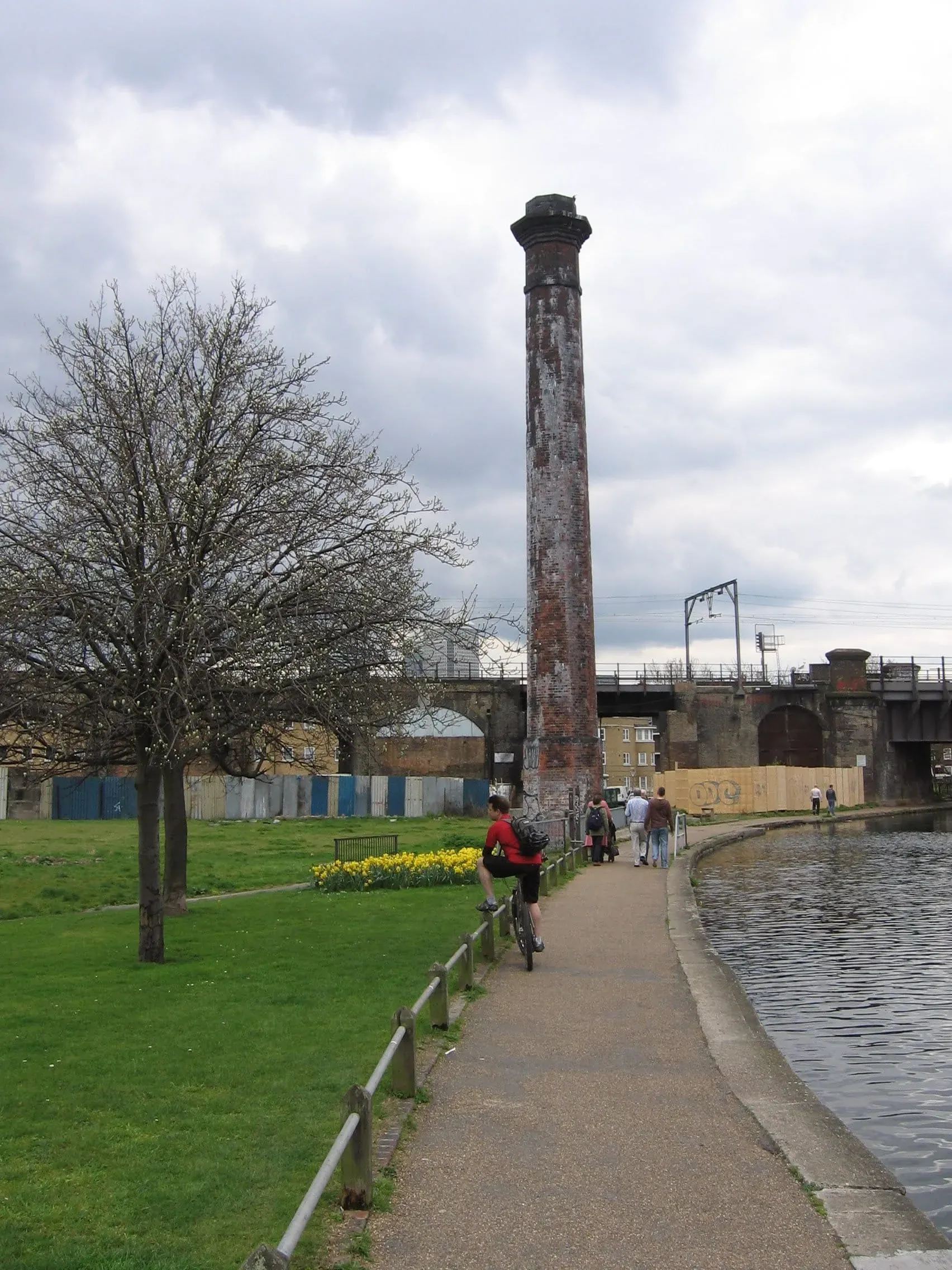 Tall brick industrial chimney beside canal towpath with cyclists and pedestrians