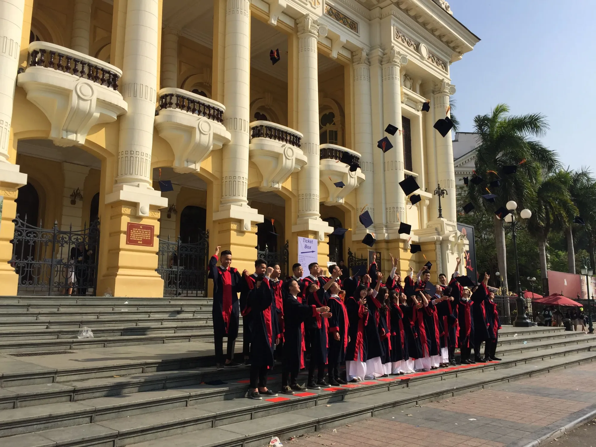 Graduates in red robes celebrate outside grand yellow building