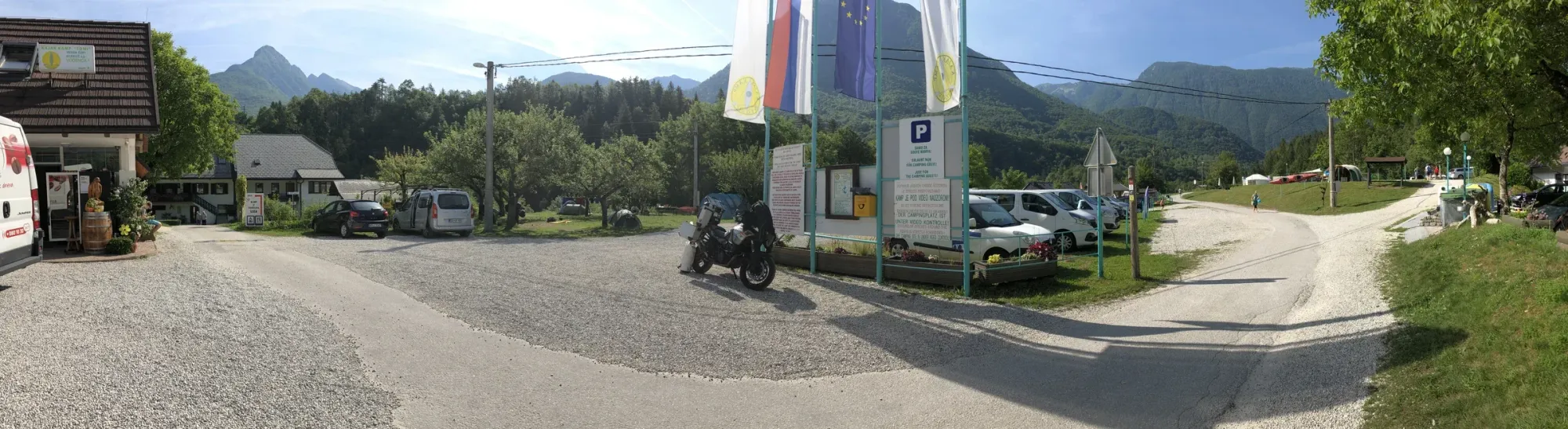 Campsite at the edge of town — Slovenian and EU flags, road bike on the gravel. Bovec, 07:33 local.