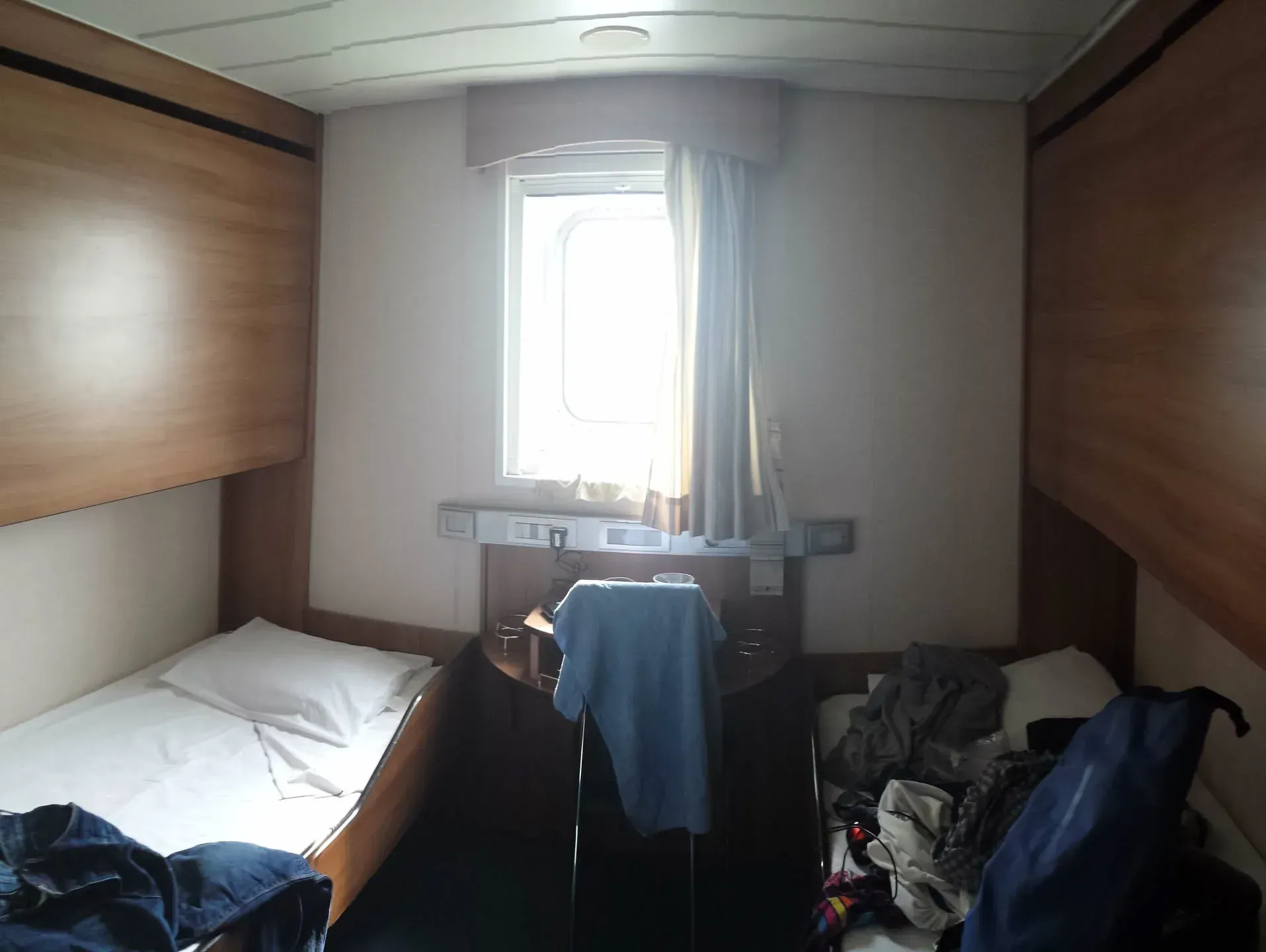 Cramped ship cabin with porthole window and scattered luggage