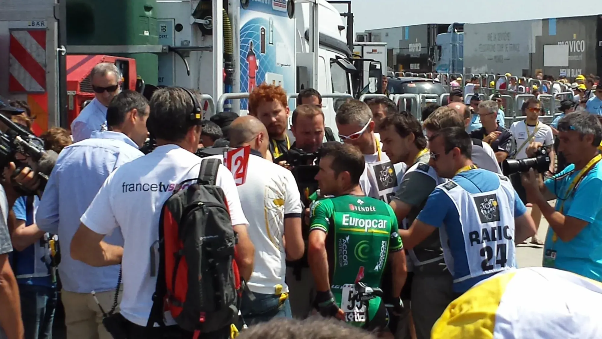 Cyclist in green jersey surrounded by media and officials