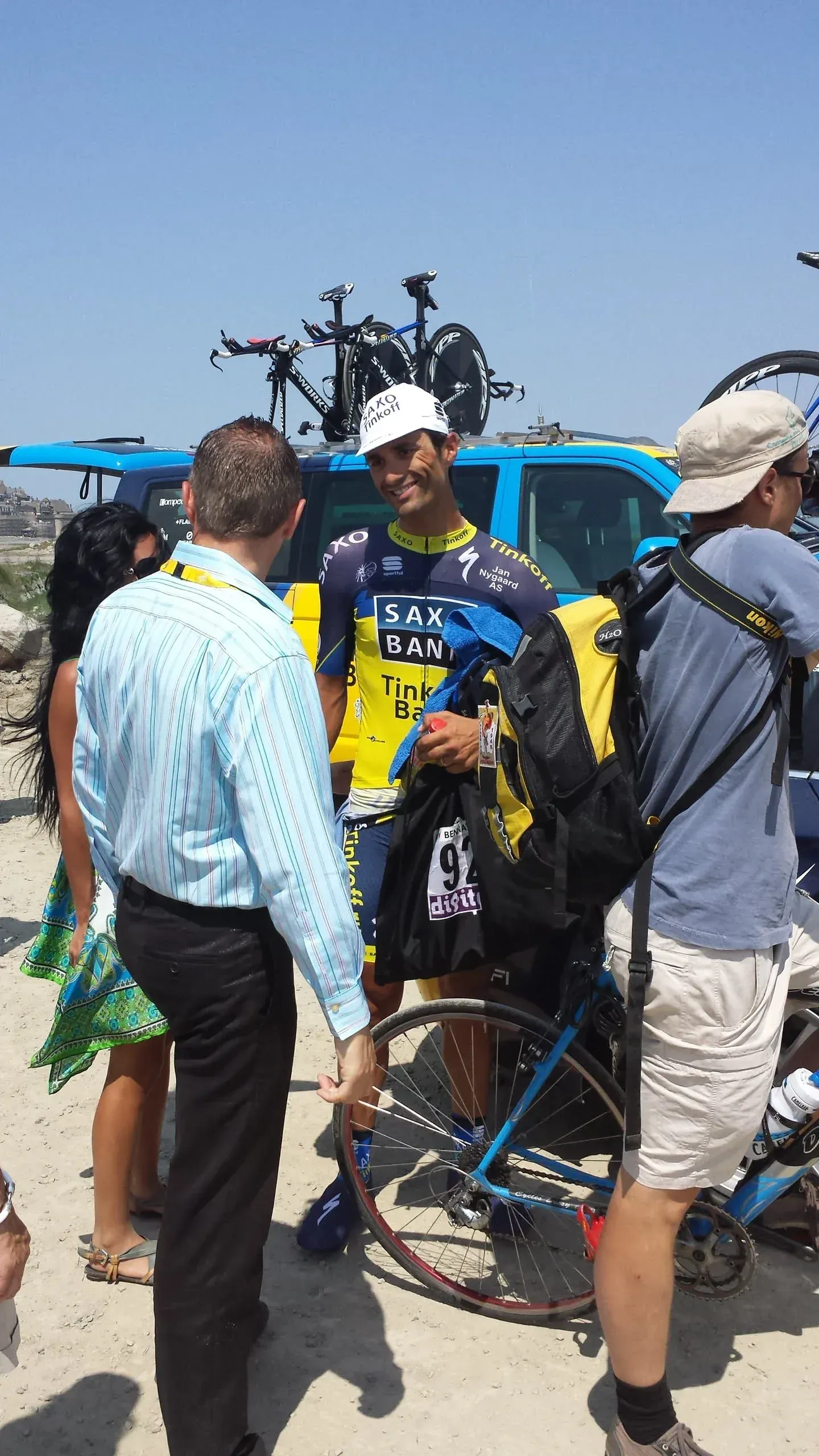 Cyclist in yellow jersey surrounded by fans and support vehicle