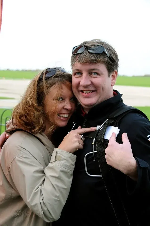 Two people smiling at camera with green fields in background