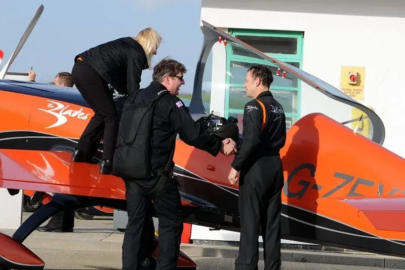 Three people in flight suits standing by red aircraft wing