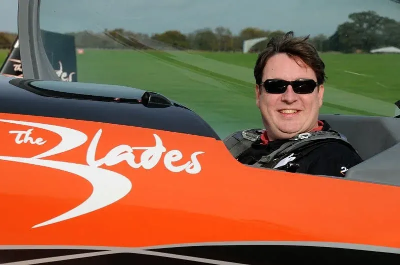 Man in sunglasses sitting in red aerobatic aircraft cockpit