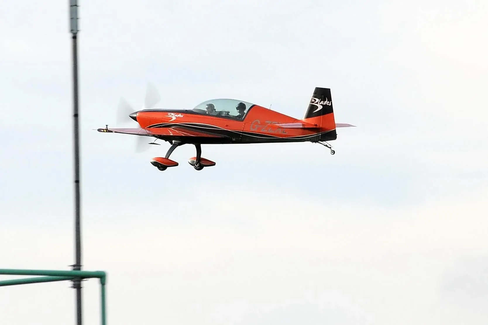 Red and black Blades aerobatic aircraft flying in cloudy sky